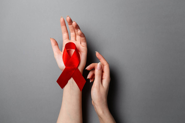 女性の手は、手のひらに赤いリボンは、エイズとの戦いのシンボルです。コピースペース。平置きだ。灰色の背景。世界エイズデーのコンセプト. - 写真・画像