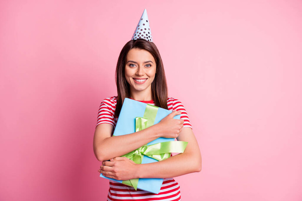 Photo portrait of happy birthday girl hugging wrapped gift wearing festive cone isolated on pastel pink color background - Foto, afbeelding
