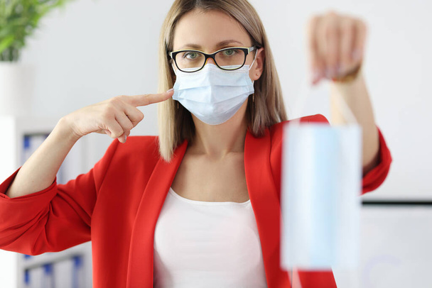 Businesswoman in red suit holding medical protective mask in office - Photo, Image