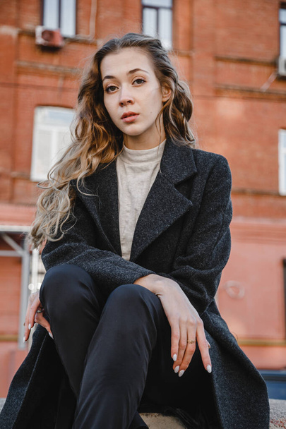 curly girl in black coat posing against background of a red building - Φωτογραφία, εικόνα