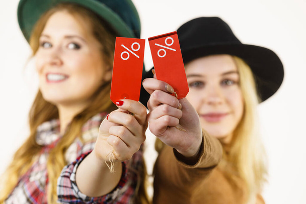 Female friends on shopping showing tag with sale percentage sign enjoying cheap clothing. - Photo, image