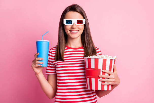 Photo portrait of happy girl wearing 3d glasses holding box with pop corn keeping cup of soda isolated on pastel pink color background - Photo, Image