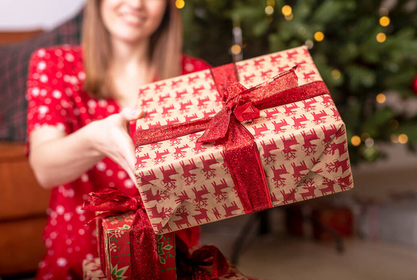 Cropped caucasuian woman holding or showing christams gift or present wrapped in paper with red ribbon and bow. Close up of a box. - Foto, immagini