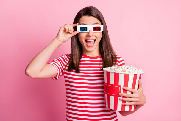 Photo portrait of girl amazed happy touching 3d glasses holding box with pop corn watching movie isolated on pastel pink color background - Foto, afbeelding