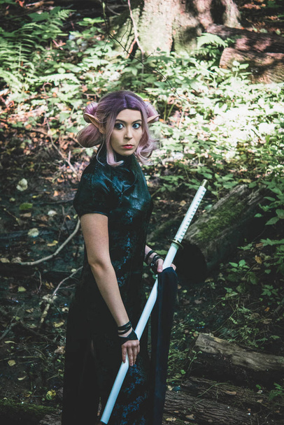 Une fille elfique avec un katana dans ses mains marche dans la forêt et se prépare pour la bataille - Photo, image