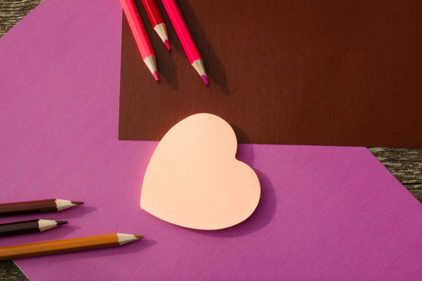 Colored pencils and stickers with pink hearts on a brown and lilac background. School stationery flat lay - Foto, imagen