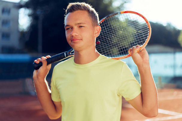 Young man teenager with tennis racket standing near net on clay court - Photo, Image