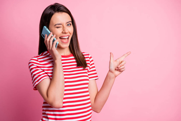 Photo portrait of girl talking on cell phone pointing finger at blank space winking isolated on pastel pink color background - Foto, Imagem