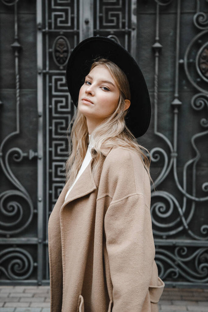 blonde in a brown coat with black hat posing, smiling, upset - Fotó, kép