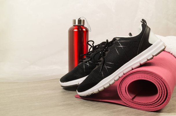 Sport equipment set. Shoes, drink bottle, towel and fitness mat on the floor. - Photo, Image