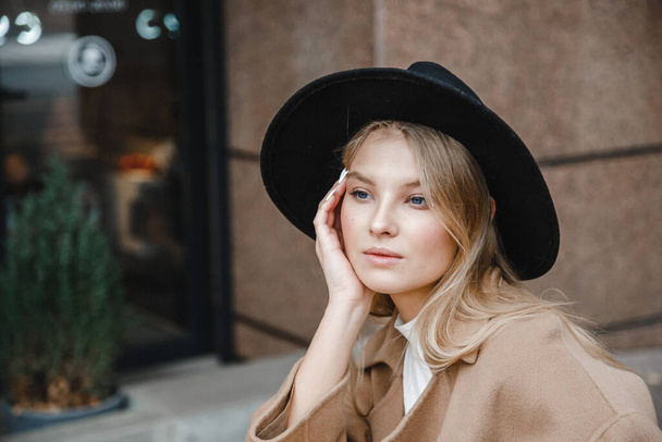 blonde in a brown coat with black hat posing, smiling, upset - Photo, Image