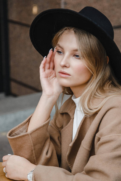 blonde in a brown coat with black hat posing, smiling, upset - Фото, изображение