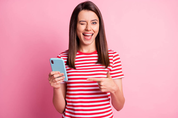 Photo portrait of girl keeping pointing at smartphone winking blinking isolated on pastel pink color background - Фото, изображение
