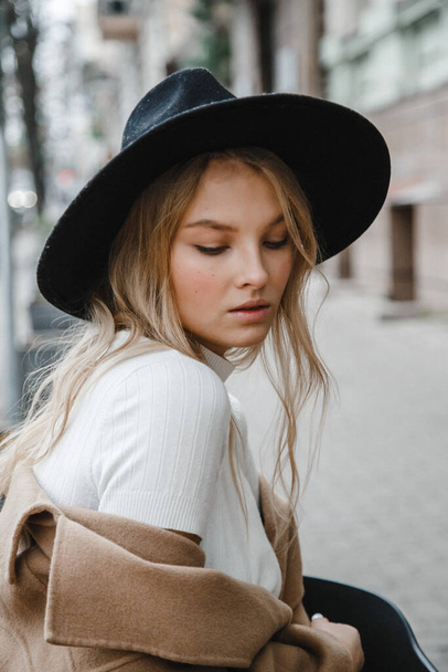 blonde in a brown coat with black hat posing, smiling, upset - 写真・画像
