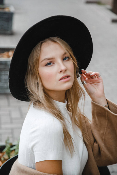 blonde in a brown coat with black hat posing, smiling, upset - Zdjęcie, obraz