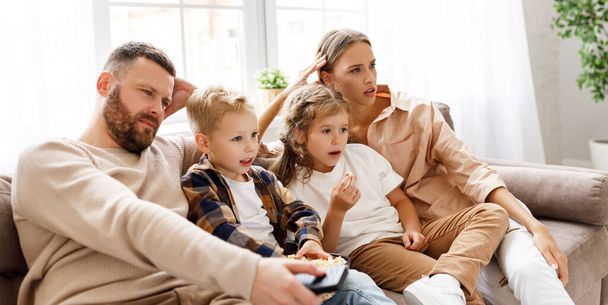 Entzückte Eltern und Kinder, die Popcorn essen, während sie auf dem Sofa sitzen und einen aufregenden actiongeladenen Film im Fernsehen sehen - Foto, Bild