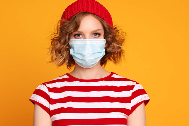 Close up portrait of young cheerful woman wearing a protective medical mask to prevent covid 19 during an outbreak of coronavirus infection on a colorful yellow backgroun - Foto, Bild