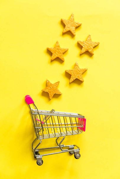 Jednoduše plochý ležel design malé supermarket nákupního vozíku pro nakupování s kolečky a 5 zlaté hvězdy hodnocení izolované na žlutém pozadí. Maloobchodní spotřebitel nákup on-line posouzení a přezkoumání koncepce - Fotografie, Obrázek