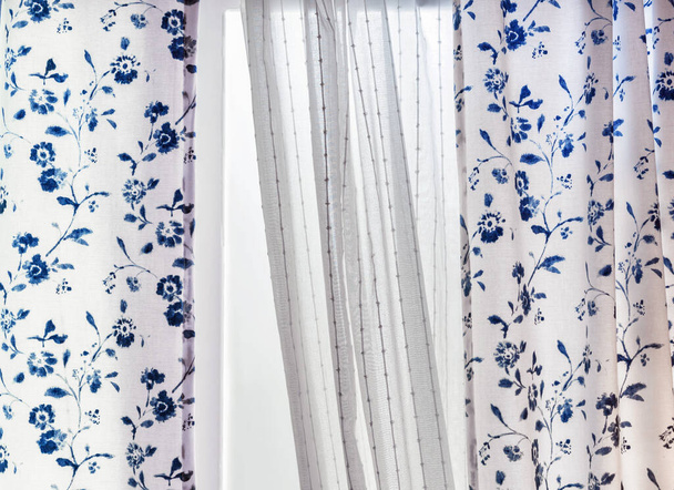Белые хлопковые шторы с синими цветочными узорами на окне гостиной. - Фото, изображение