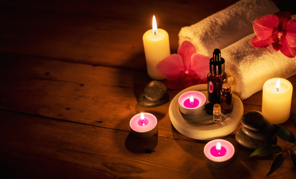 spa romántico - aceites esenciales con piedras de masaje y flores en cadlelight sobre fondo de madera con espacio de copia - Foto, Imagen
