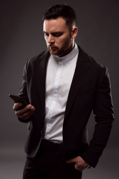 a young brutal businessman writes a message on a smartphone, a close-up photo on a dark background - Foto, Bild