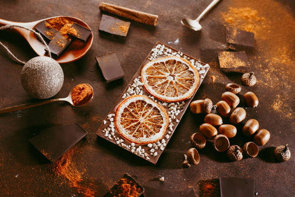 Composition of bars and pieces of different dark chocolate with orange slices, spices on a brown background close - up view from above - Foto, afbeelding