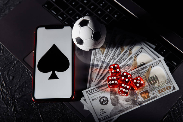 Dice, soccer ball, smartphone and dollar banknotes on keyboard. Gambling addiction and betting concept - Photo, Image