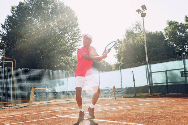 Middle-aged man playing tennis on outdoor tennis filed - Фото, изображение