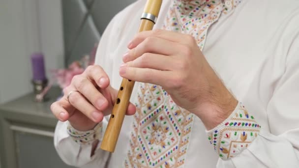 Un uomo che suona il flauto flauto registratore in legno. Il musicista è vestito con una bella camicia ricamata - Filmati, video
