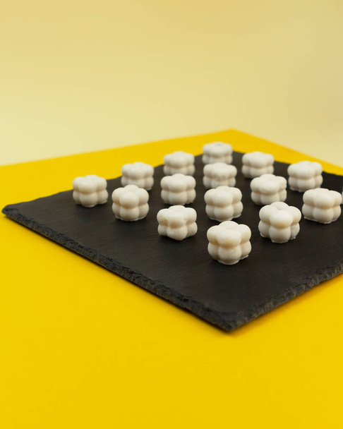 Homemade coconut manna sweets. Modern shape on a geometric yellow background. A fat bomb for the ketogenic diet. - Foto, afbeelding