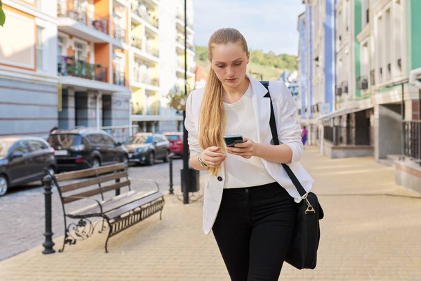 Young business woman with smartphone walking along city street - Fotoğraf, Görsel