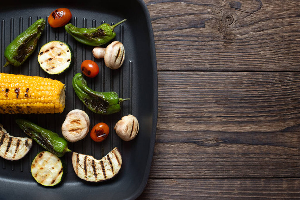 Gebakken, gebakken, gestoomde groenten op een grillpan op een houten tafel. Grillmenu. Kopieerruimte. - Foto, afbeelding