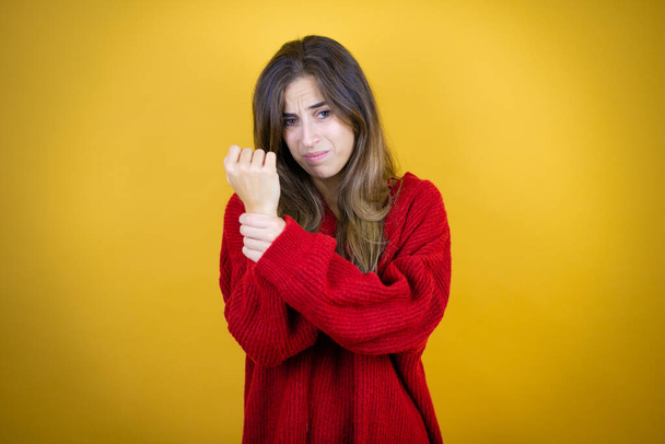 Молода красива жінка в червоному светрі над ізольованим жовтим тлом страждає від болю на руках і пальцях, запалення артриту
 - Фото, зображення