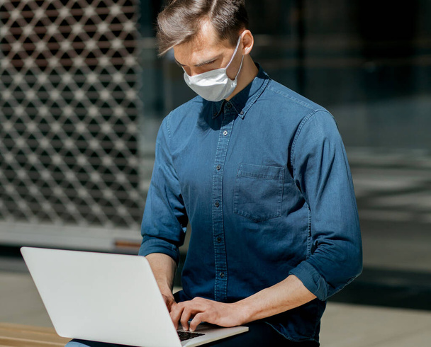 close up. city guy in a protective mask is working on a laptop - Fotó, kép
