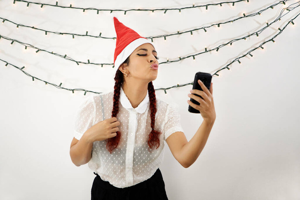 Fille avec un chapeau de Noël rouge et les cheveux roux, avec un téléphone portable faire un appel vidéo, souffler un baiser. Belle fille - Photo, image