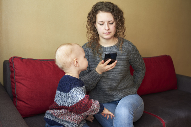 Moeder is onverschillig voor haar zoontje, moeder kijkt naar de smartphone, het kind heeft aandacht nodig. Het thema van ouder-kind relaties. - Foto, afbeelding