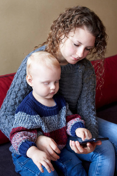 Mutter zeigt ihrem kleinen Sohn, wie man ein Handy benutzt, die frühe Entwicklung des Kindes. - Foto, Bild