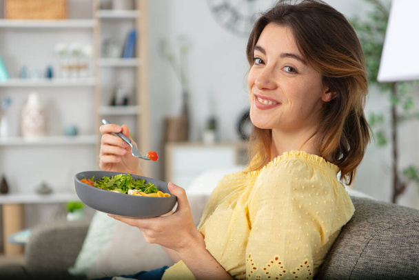 woman sat at home eating a bowl of salad - Foto, afbeelding