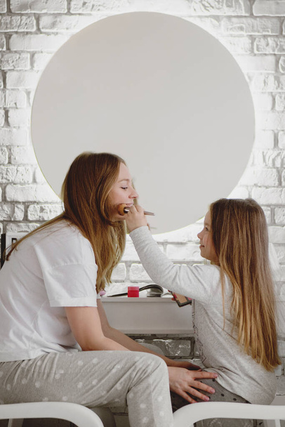 Close up portrait of little girl doing makeup to her mom. - 写真・画像