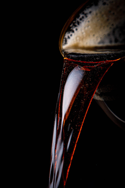 Black beer pouring on a black background - Foto, Imagem