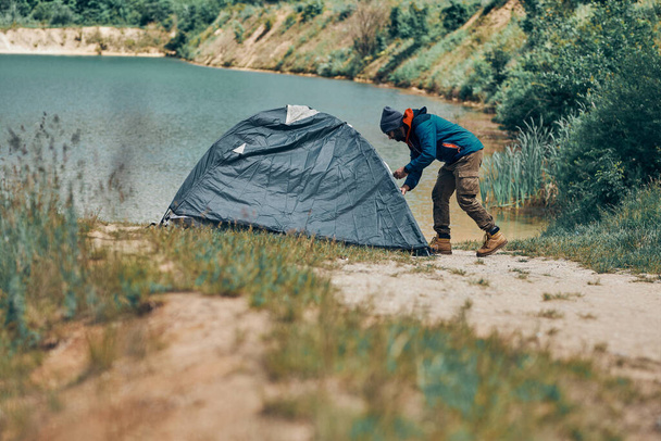 Un explorador ajustando la tienda en la orilla del lago. - Foto, Imagen