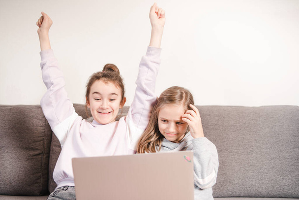 Una chica está contenta con otra triste mirando a la computadora.Dos niñas se dedican a la educación a distancia. Enseñanza en casa. Educación en el hogar. - Foto, Imagen