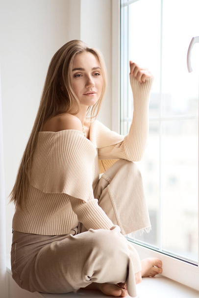 Concept People and Activity. A young caucasian woman sits on the window sill in the early morning. - Photo, Image