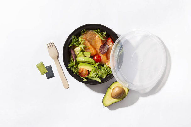 neem weg doos met zalmsalade een avocado en vork op witte achtergrond - Foto, afbeelding
