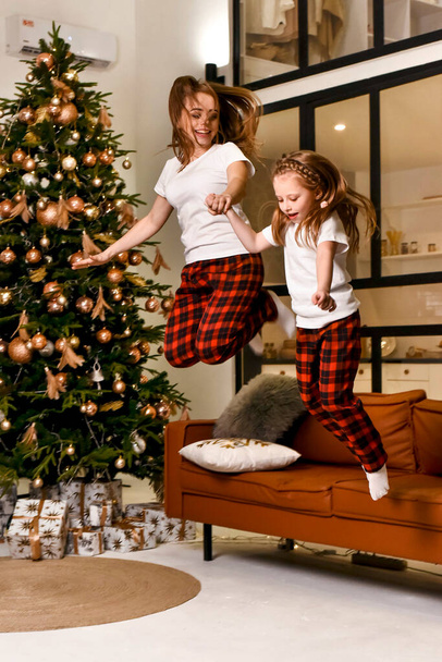 Mom and daugher are jumping near the Christmas tree - Foto, Imagen