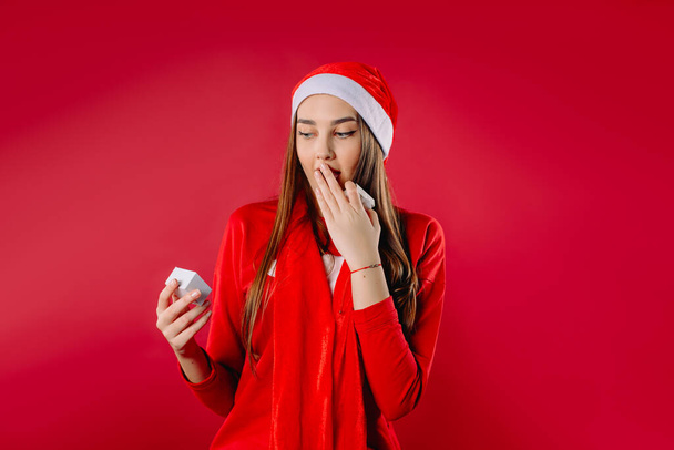 A cute girl holds her hand to her face, surprised by a gift in a small box. High quality photo - Foto, afbeelding