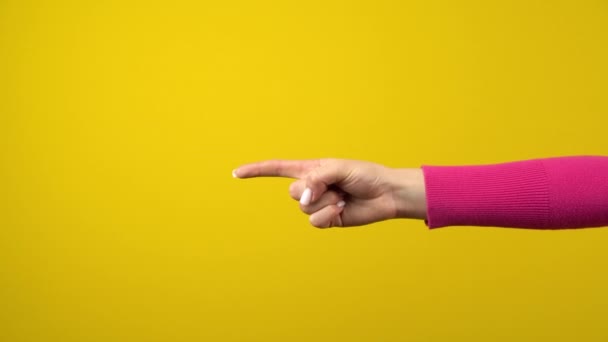 The female hand shows the index finger to the empty space. Studio shooting on an isolated yellow background. - Footage, Video