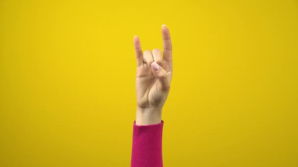 Vrouwelijke hand toont het teken van de hoorns. Studio fotografie op een geïsoleerde gele achtergrond. - Video