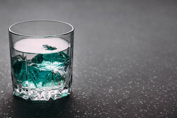 Gin in a glass on a black background with blue ice cubes on a wooden surface. Alcohol with ice. Place for an inscription. - Valokuva, kuva
