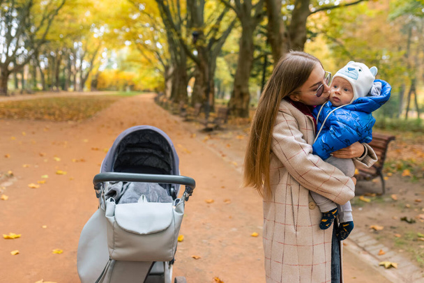 Mamá besa a su bebé mientras se sostiene en brazos mientras camina en el parque - Foto, Imagen